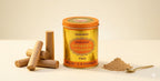 Gold-colored container of Shree Kashi Maharaja Chandan Tika with wooden sticks and powder on a beige background