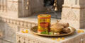 Candle labeled 'Maharaja Chandan' on a decorative tray with sandalwood and other items in front of an architectural background.