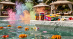 Colorful powder cans and a box by a pool with flowers and colorful smoke.