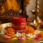 Red jar with gold text on a tray with flowers and a lit candle