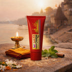Red tube of Kashi Chandan Tika with traditional elements on a stone surface with a sunset background.