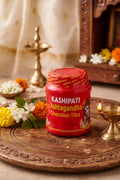 Red jar labeled 'Kashipati Ashtagandha Chandan Tika' on a wooden tray with decorative elements.